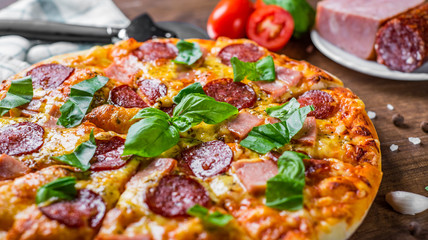 Pepperoni Pizza with Mozzarella cheese, salami, ham, Spices and Fresh basil. Italian pizza on wooden table background