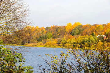 Beautiful autumn landscape with autumn leaves on trees branches on a background of the river, colorful autumn forest and blue sky. Autumn scene. Nature concept. Outdoor recreation concept.