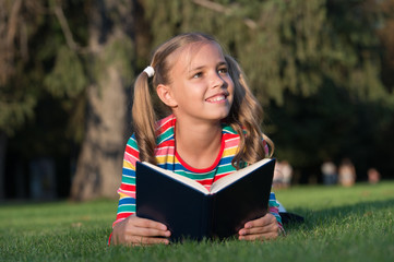 Little child reading book outdoors. Schoolgirl reading stories while relaxing green lawn. Cute pupil enjoy reading. School time. Developing caring learners who are actively growing and achieving