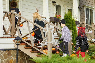 Full length portrait of children trick or treating on Halloween standing on porch, copy space