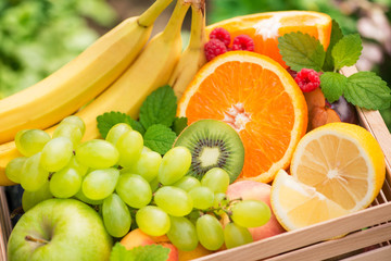 Basket of fresh fruits with banana, apple, grapes, green kiwi in the garden background