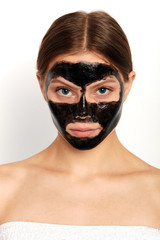 attractive girl has applied a black mask on her face, close up portrait, studio shot. isolated white background. studio shot