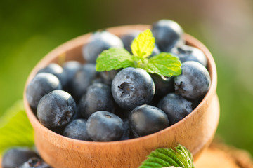 Fresh and natural blueberry with mint leaf on a stump green garden background