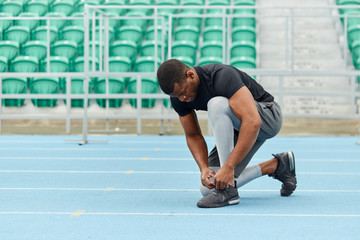 african guy tying shoelaces at the stadium, green seats in the background of the photo. full length side view photo. free time, spare time, copy space © alfa27