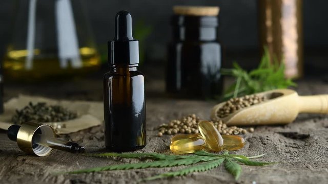 hemp essential oil in small glass bottle. container with cannabis leaves and cannabis seeds on wooden.