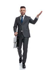 happy young businessman walking and welcoming while holding suitcase