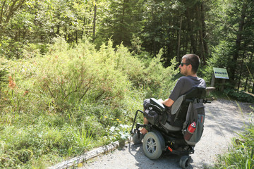 Fototapeta na wymiar Happy man on wheelchair in nature. Exploring forest wilderness on an accessible dirt path.