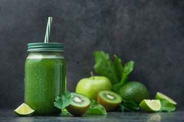 Green detox smoothie in glass jar from spinach, kiwi, lime, avocado on a dark stone table