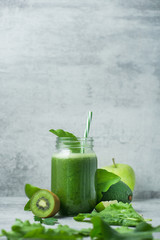 Green detox smoothie in glass jar from spinach, kiwi, lime, avocado on a light stone background