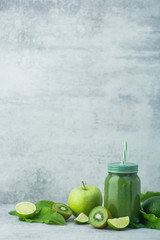 Green detox smoothie in glass jar from spinach, kiwi, lime, avocado on a light stone background