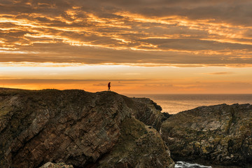 Fototapeta premium Person in shadow walking in a cliff on a sunset with an impresive orange sky