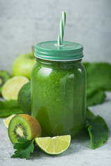 Green detox smoothie in glass jar from spinach, kiwi, lime, avocado on a light stone background