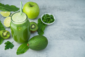 Green detox smoothie in glass jar from spinach, kiwi, lime, avocado on a light stone background