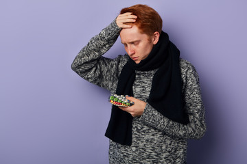 man with terrible headache holding many pills, cannot decide whic of them is more effective. close up portrait, isolated blue background, studio shot