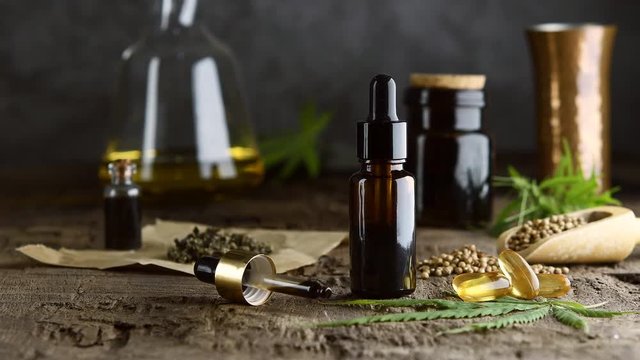 hemp essential oil in small glass bottle. container with cannabis leaves and cannabis seeds on wooden.