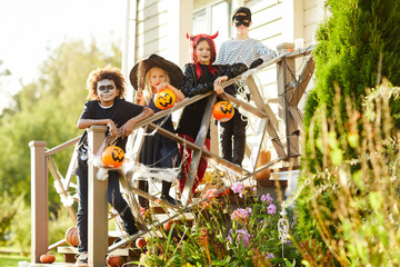 Multi-ethnic group of children wearing Halloween costumes standing on stairs of decorated house...