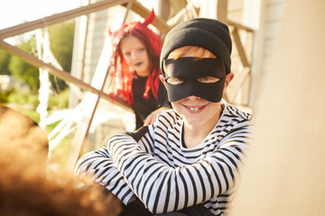 Portrait of cute little boy wearing Halloween costume looking at camera while sitting outdoors with friends, copy space