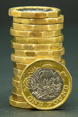 Stack of one British pound coins with single coin facing front standing on its edge at the bottom of the pile