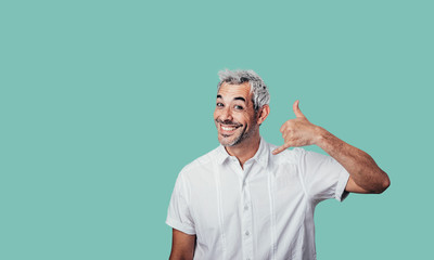 Human facial expressions concept. Call me back please! Young attractive guy in casual t shirt, makes phone sign, wants to speak with someone via cell phone. Body language concept.