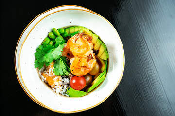 Salad with fried shrimp, rice, avocado, green beans and cherry tomatoes in a yellow bowl on a dark background. Seafood. Healthy and wholesome food. Buddha Bowl
