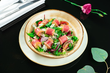 Fresh and delicious Tataki salad with tuna, lettuce, red onion, cherry tomatoes and daikon radish. Tasty seafood salad of Japanese cuisine in yellow bowl on dark background. Close up food photo