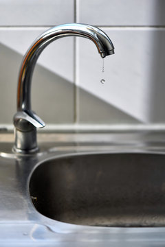 Clean water drops falling from a dripping kitchen faucet, an unnecessary waste of water in a world threatened by water scarcity.