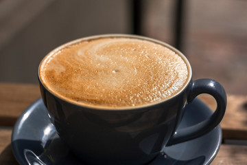 Blue round cup of latte coffee on a plate on the cafe wooden table outside.