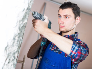 Naklejka premium attentive builder drilling hole in wall with perforator