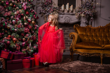 little blonde girl in evening red dress near the Christmas tree, child with Christmas gifts, the night before Christmas