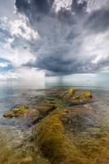 crystal clear water with green mossy stones at Lake Malawi, dark stormy clouds in the sky, Africa
