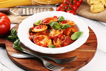 Ravioli with tomato sauce garnished with parmesan cheese and basil on rustic table