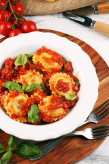 Ravioli with tomato sauce garnished with parmesan cheese and basil on rustic table
