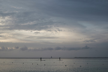 Paddle boarder heading offshore at dusk on the calm waters off the Cayman Islands