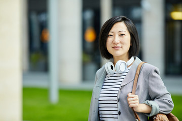 Waist up shoulders portrait of modern Asian woman looking at camera while posing outdoors in city street, copy space