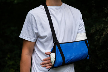 Man with broken arm wrapped medical cast plaster and blue bandage. Fiberglass cast covering the wrist, arm, elbow after sport accident, isolated on black