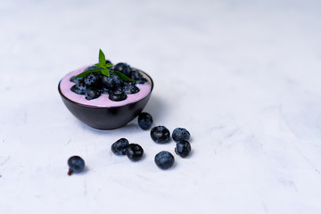 Tasty fresh blueberry yoghurt shake dessert in ceramic bowl standing on white table background.