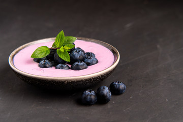 Tasty fresh blueberry yoghurt shake dessert in ceramic bowl standing on black dark table background.