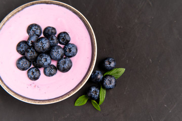 Tasty fresh blueberry yoghurt shake dessert in ceramic bowl standing on black dark table background.