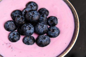 Tasty fresh blueberry yoghurt shake dessert in ceramic bowl standing on black dark table background.