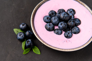 Tasty fresh blueberry yoghurt shake dessert in ceramic bowl standing on black dark table background.