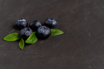 blueberries with green leaves lie on dark black background.