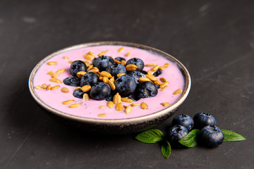 Tasty fresh blueberry yoghurt shake dessert in ceramic bowl standing on black dark table background.