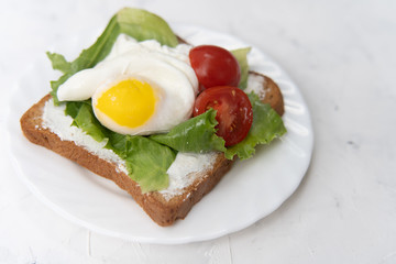 Sandwich with fried eggs salad and tomato on a white plate on a white background.