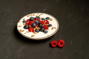 Tasty fresh blueberry raspberries  yoghurt shake dessert in ceramic bowl standing on black dark table background.