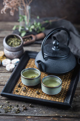 Still-life of japanese healthy green tea in a small cups and teapot over dark background
