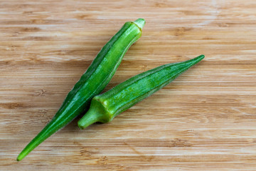 Two green okras on a brown wooden surface, side view from above