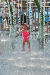 Portrait of a little girl of one year old on water rides. She is dressed in a pink swimsuit and hat, smiles cheerfully and plays with water drops.