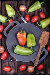 Cast iron pan with vegetables on dark wooden table in rustic style. Organic food. Tomatoes, onions and bell peppers. Flat lay