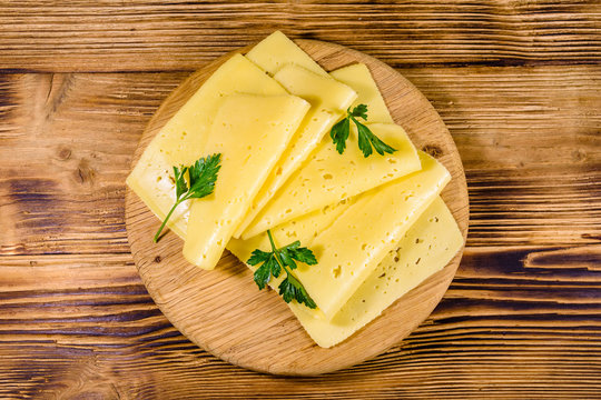 Sliced cheese and parsley on a wooden cutting board. Top view