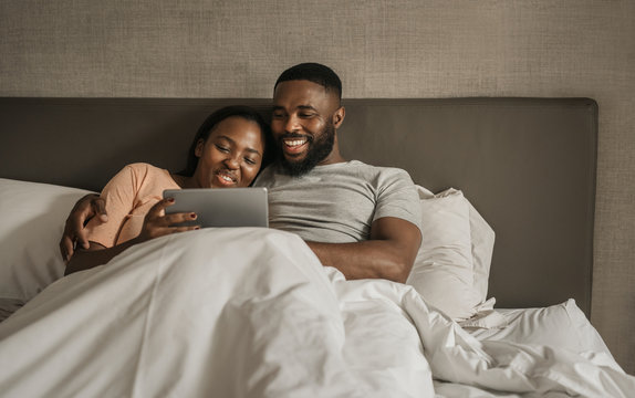 Smiling young African American couple using a tablet in bed